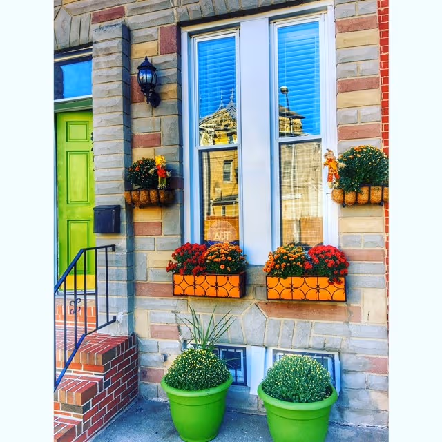 Front entrance of a brick building with a green door and colorful planters.