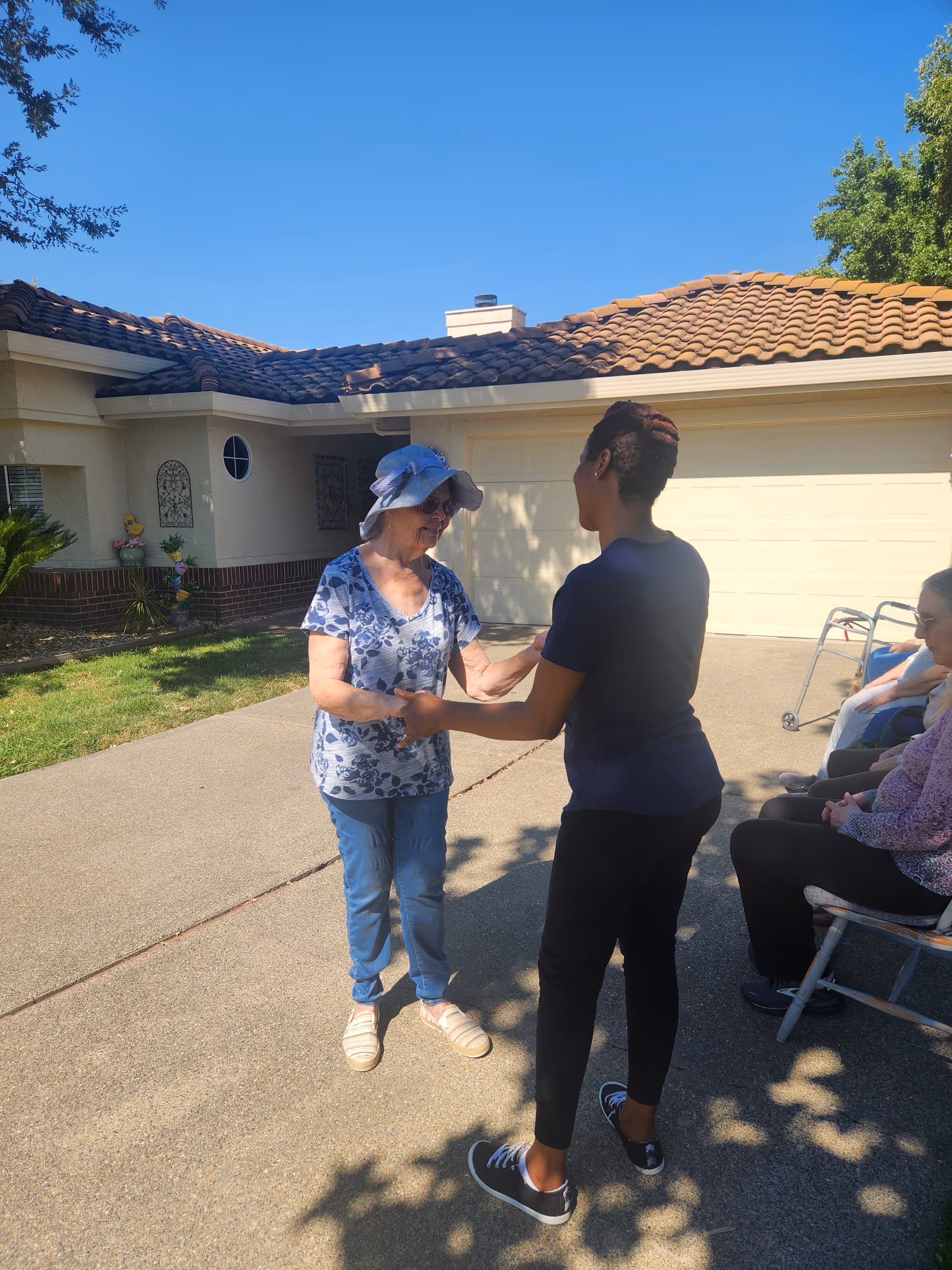 Two people greet each other outside Woodcreek Villa with residents nearby.