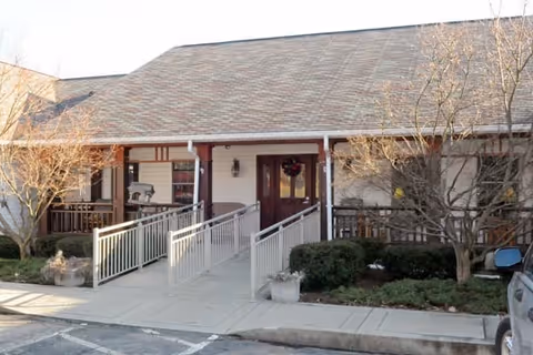 Exterior view of the entrance to Concordia of Wexford facility featuring a covered porch with a ramp and stairs, surrounded by shrubs and leafless trees, with a parked vehicle partially visible on the right.