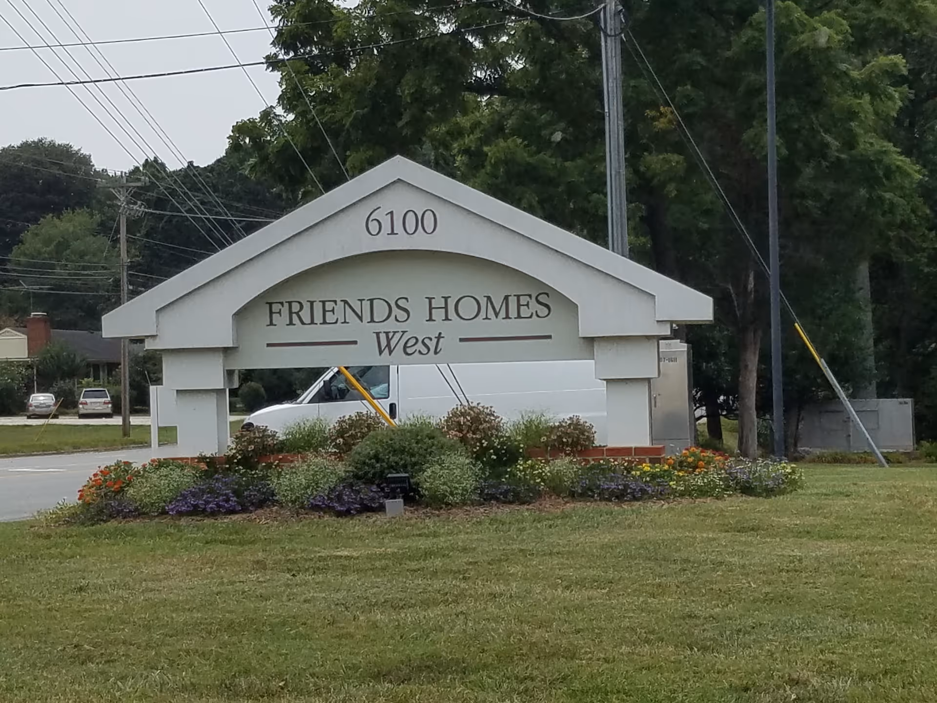 A large arch-shaped entrance sign reading Friends Homes West with colorful flower beds in front.
