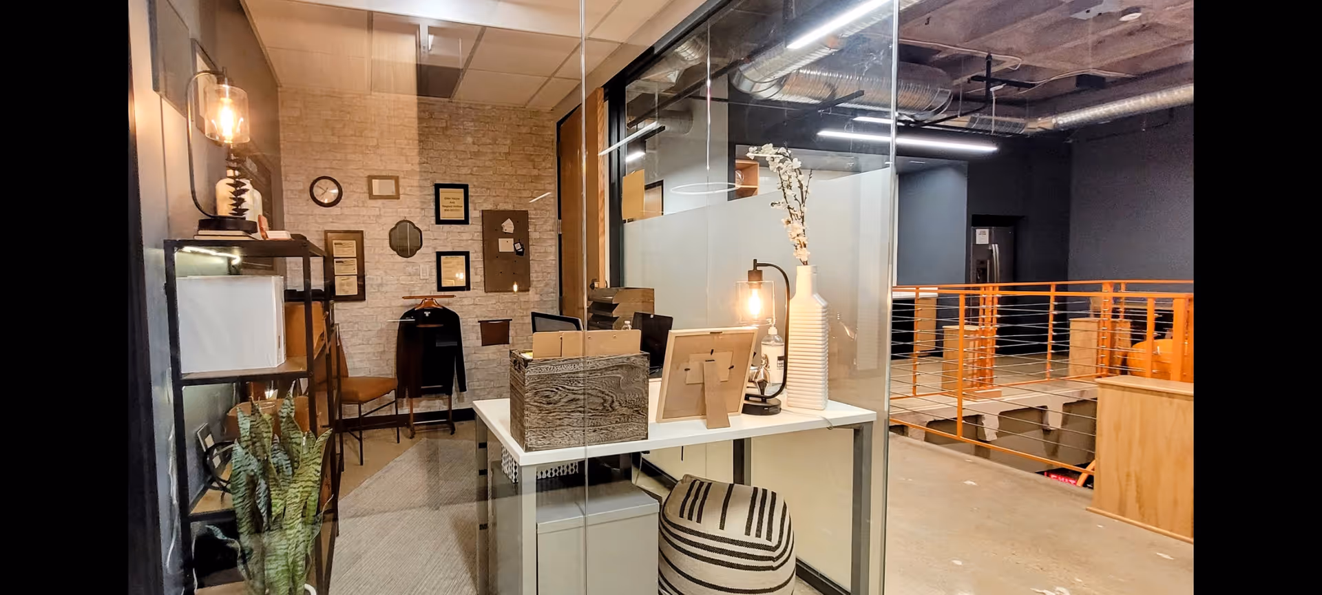 Interior reception area with glass partition, desk, plants, and warm lighting.