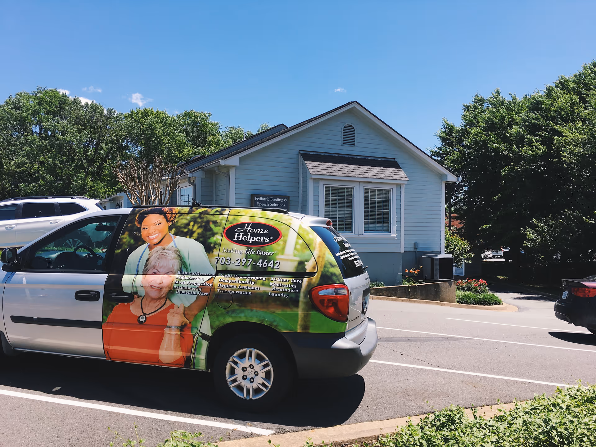 Blue single-story senior care facility with a branded van in a parking lot.