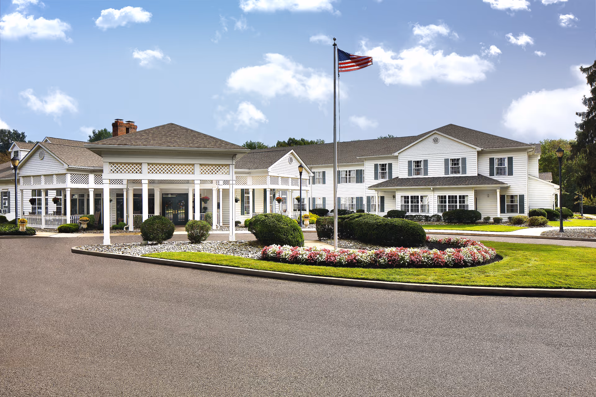 Exterior view of a white senior living campus with a circular driveway and flagpole.