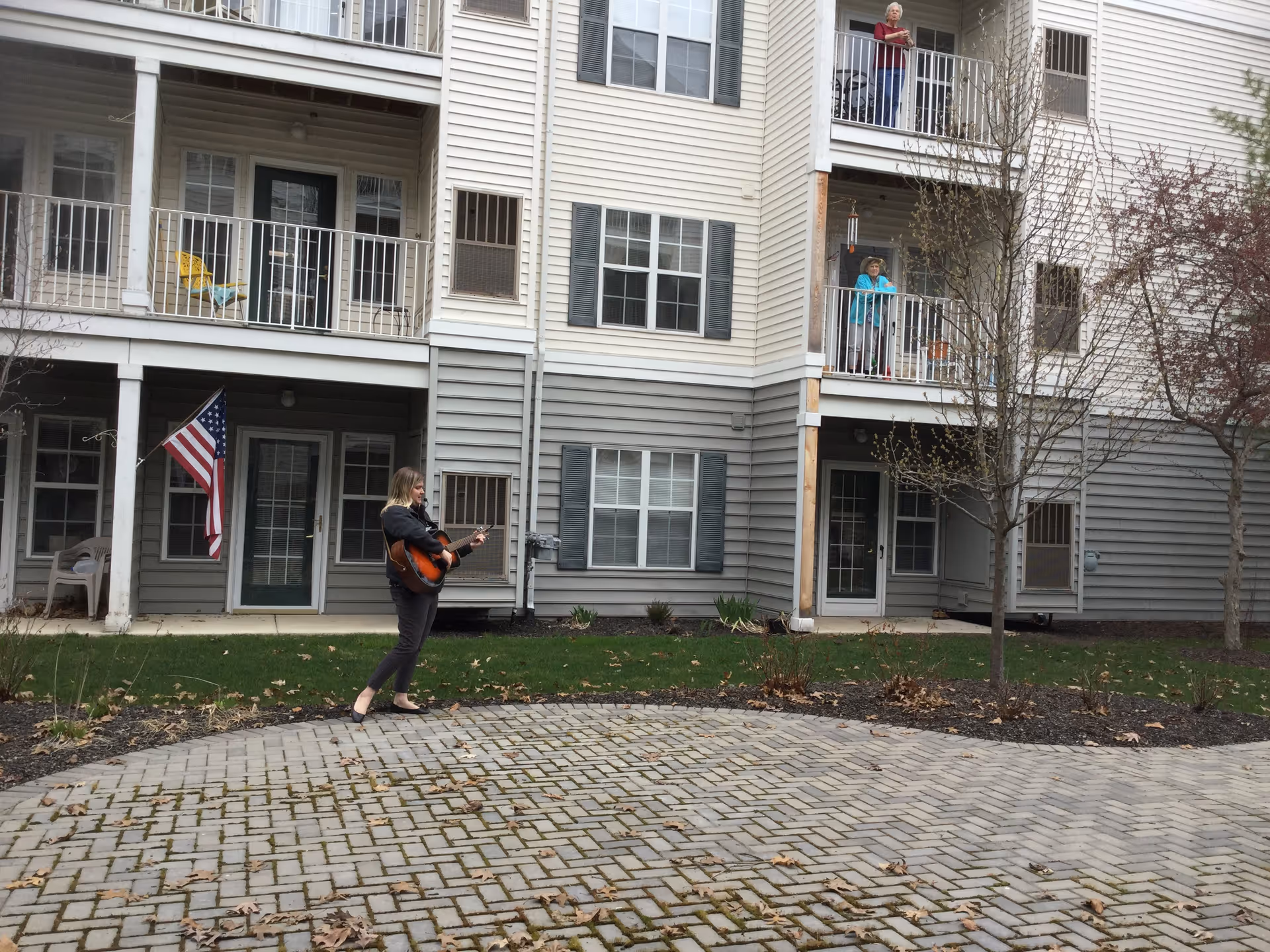 Guitarist performs outside a senior living building with residents on balconies.