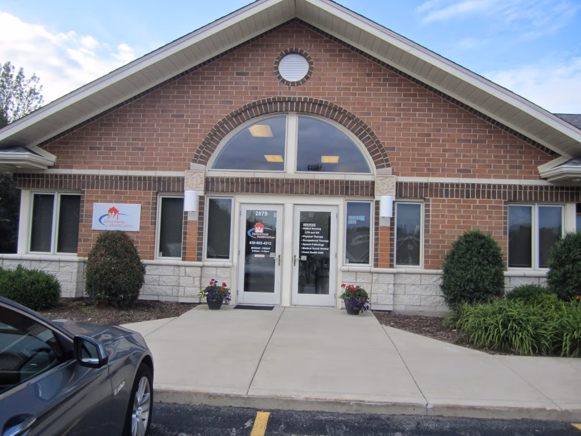 Brick facility front with arched window, glass doors, sign, and parked car.