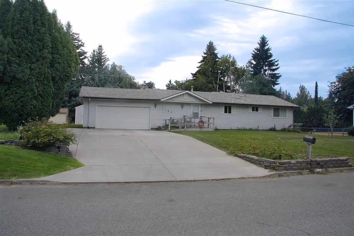 A single-story white home with attached two-car garage, driveway, and well-kept lawn.