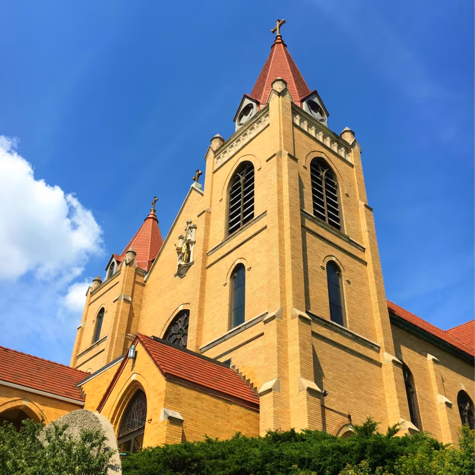 Tall brick church with red-tiled roofs and twin steeples against a clear blue sky.