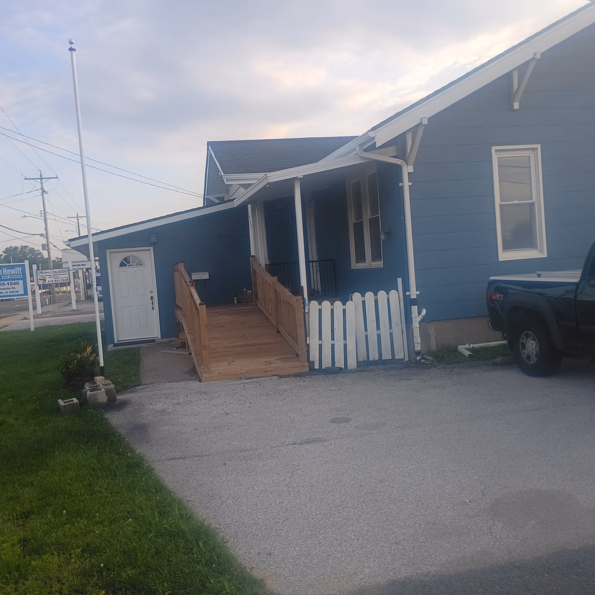 Blue single-story building exterior with wooden ramp and white picket fence.