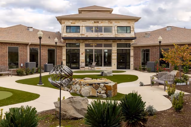 Well-maintained courtyard with walkways, benches, landscaping and a central rock fountain in front of a brick building entrance.