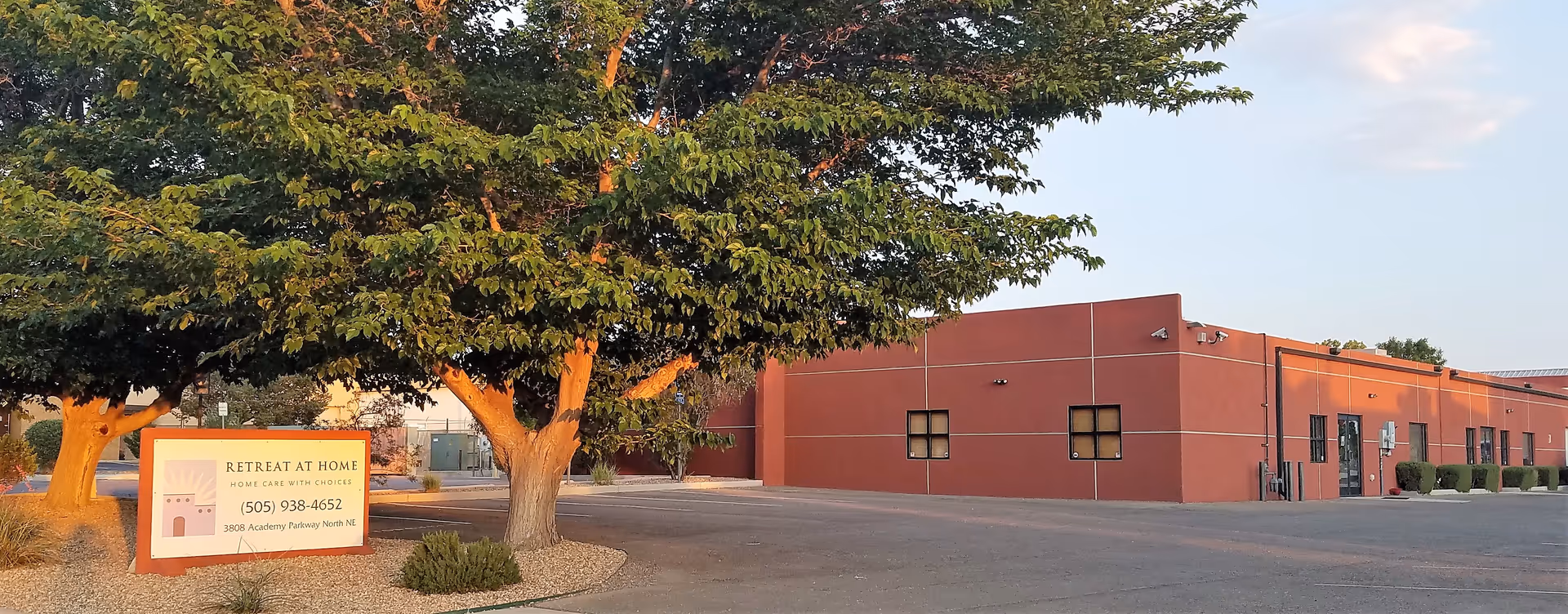 Exterior view of a red-orange building with a Retreat At Home sign and trees