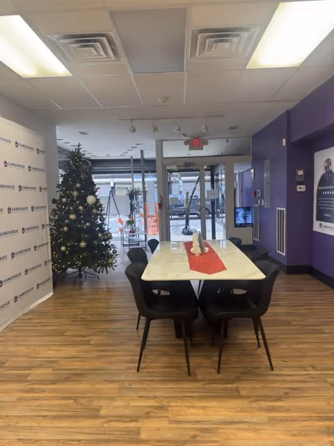 A long white table with black chairs in a purple-walled dining area and Christmas tree.