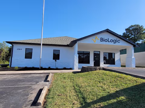 White single-story building with BioLogic sign, glass doors, and a small grassy front yard.