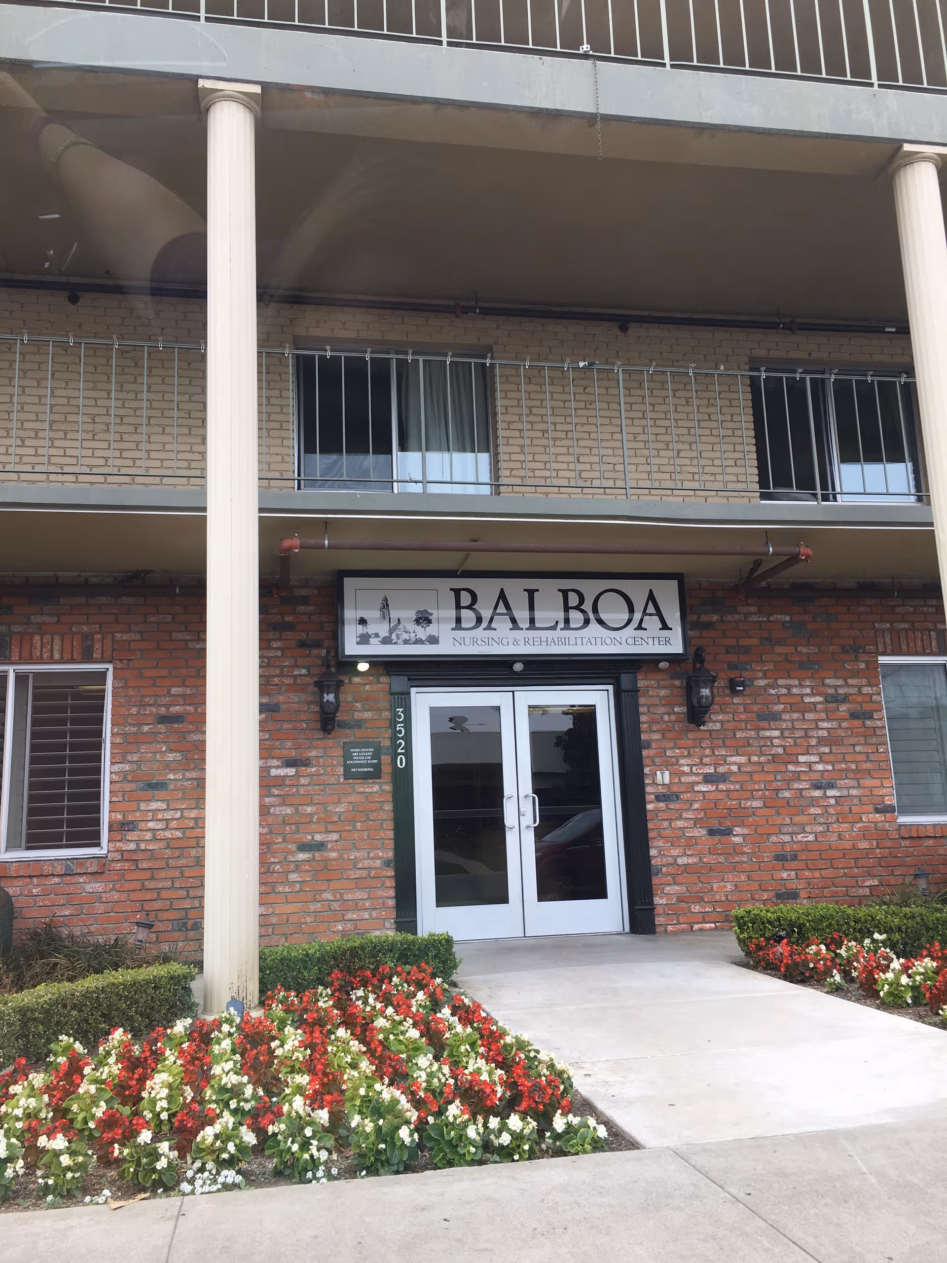 Front entrance of Balboa Nursing and Rehabilitation Center with brick exterior and blooming flowers.