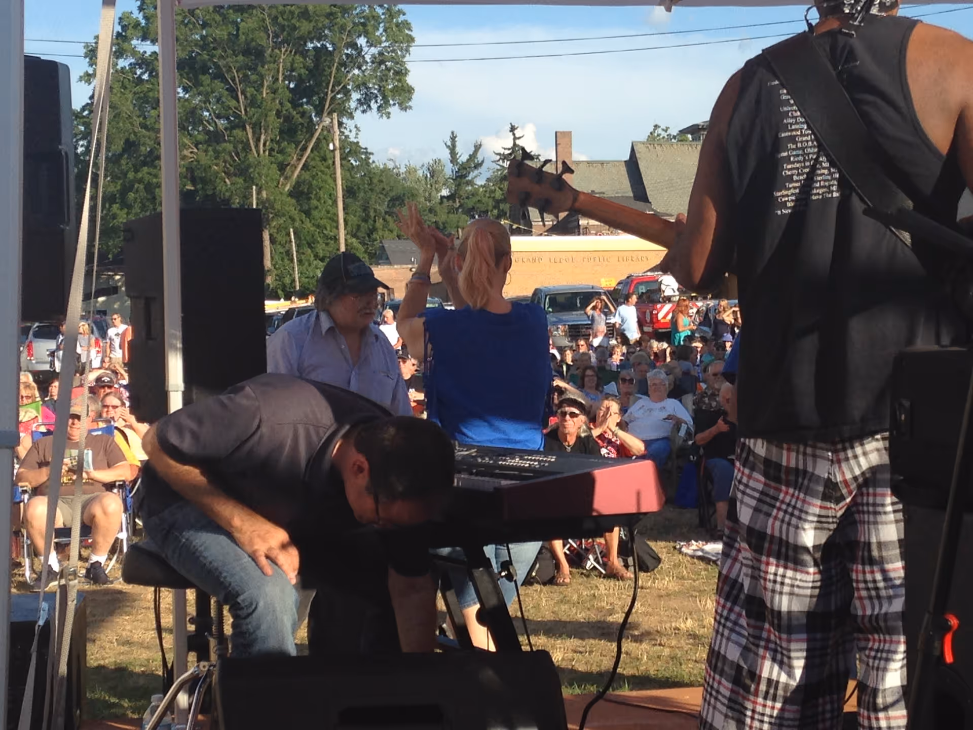A live outdoor concert with musicians performing on stage and a crowd watching.