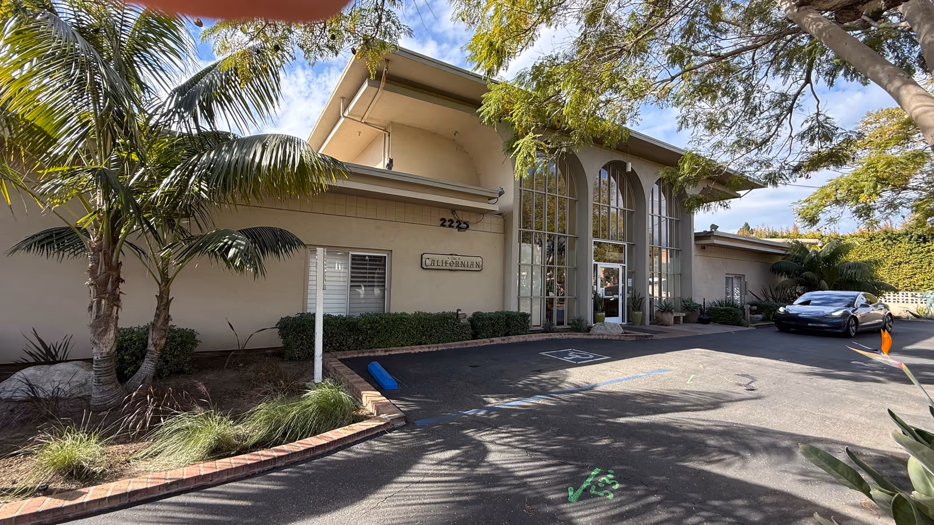 Exterior view of The Californian senior living entrance with parking and palm trees.