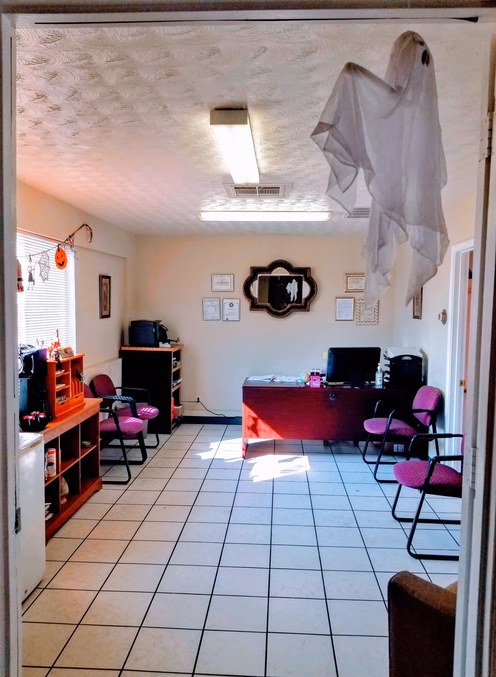 Office reception area with desk, chairs, framed certificates, and decorations.