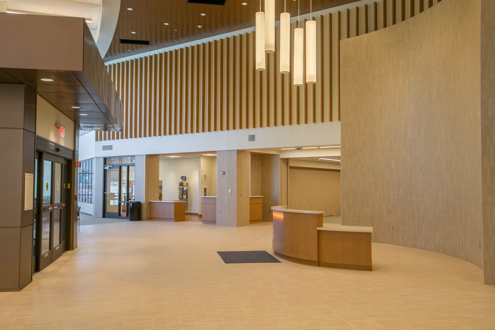 Spacious hospital lobby with curved reception desk, tall wooden slats, and pendant lights.