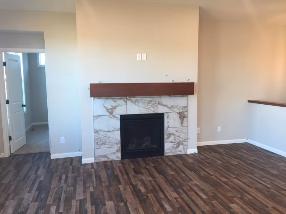 Interior living room with marble fireplace, beige walls, and hardwood flooring.