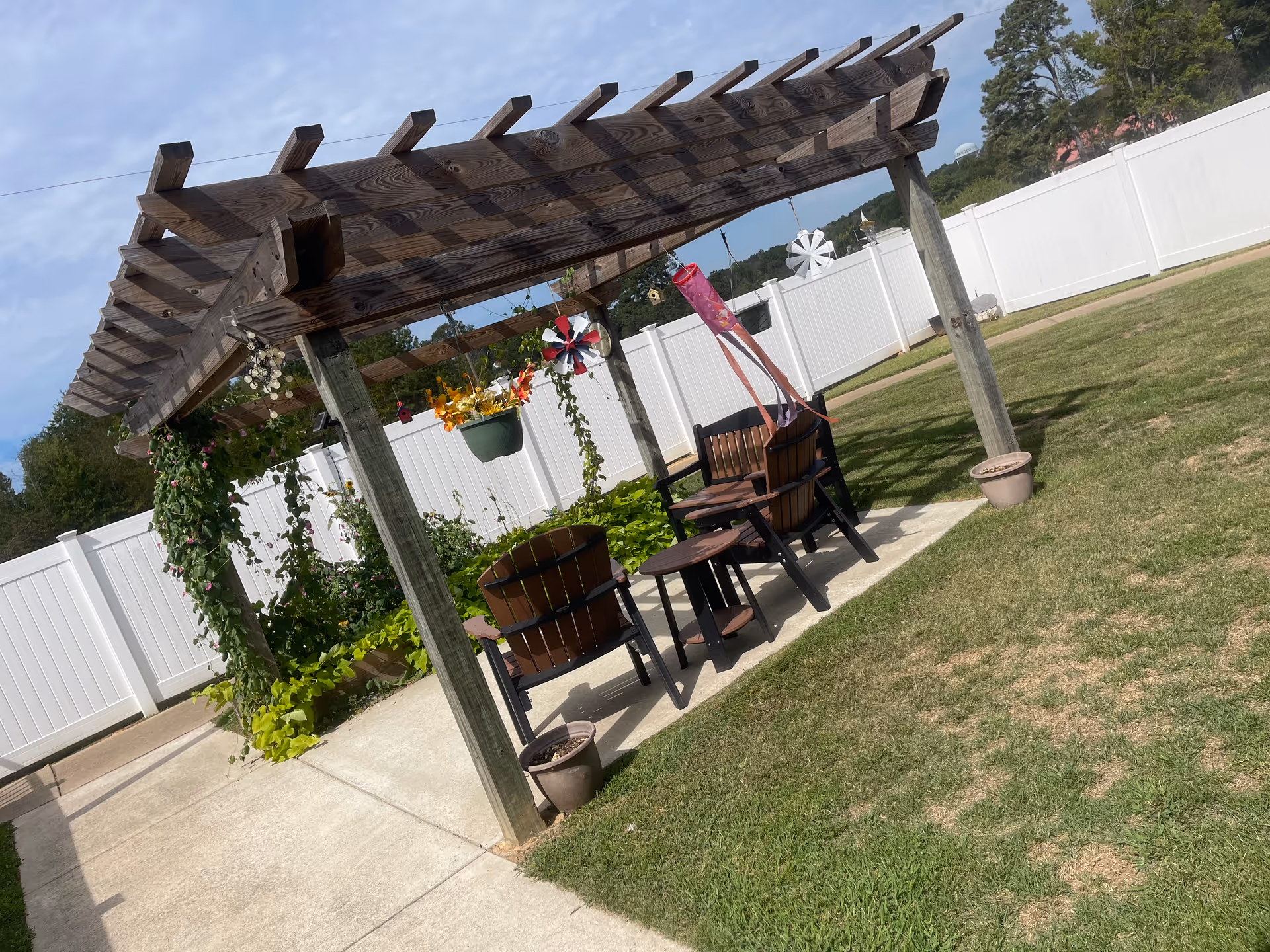 Outdoor pergola seating area with chairs, potted plants, and hanging baskets.
