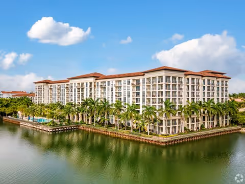 Waterfront senior living building with palm trees and a pool along the water.