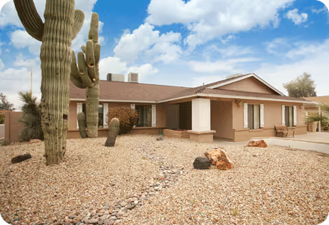 Single-story beige senior home with desert landscaping and tall cacti at the entrance.