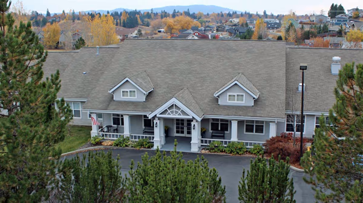 Front exterior of a single-story residential-style building with a covered entrance, driveway, and surrounding trees.
