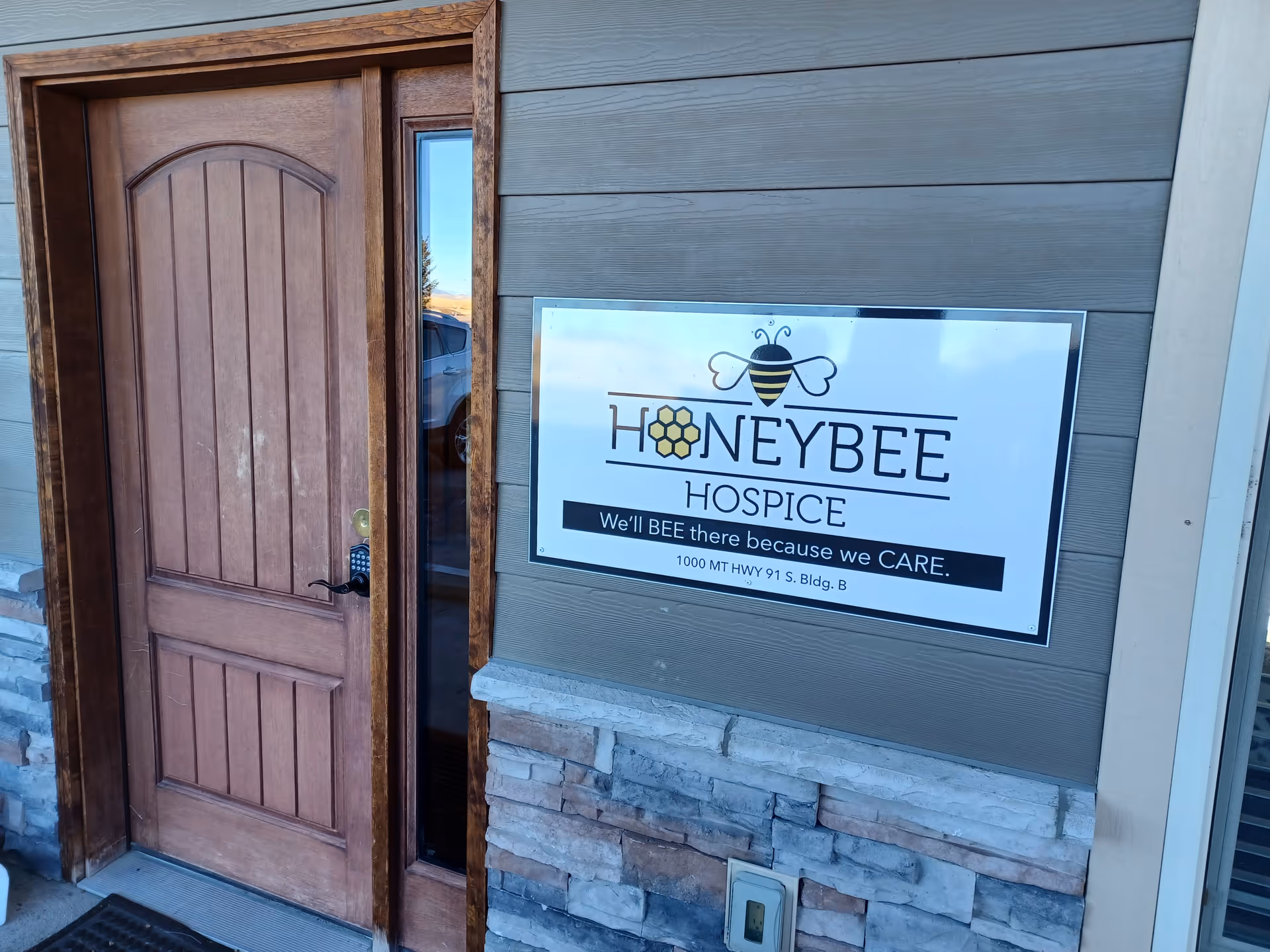 Exterior view of Honeybee Hospice entrance with wooden door and campus sign.