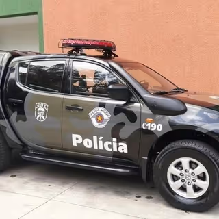Police SUV with crest emblems and red light bar parked beside a peach-colored exterior wall.