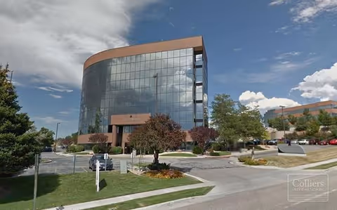 Exterior view of a curved glass building with parking and trees.