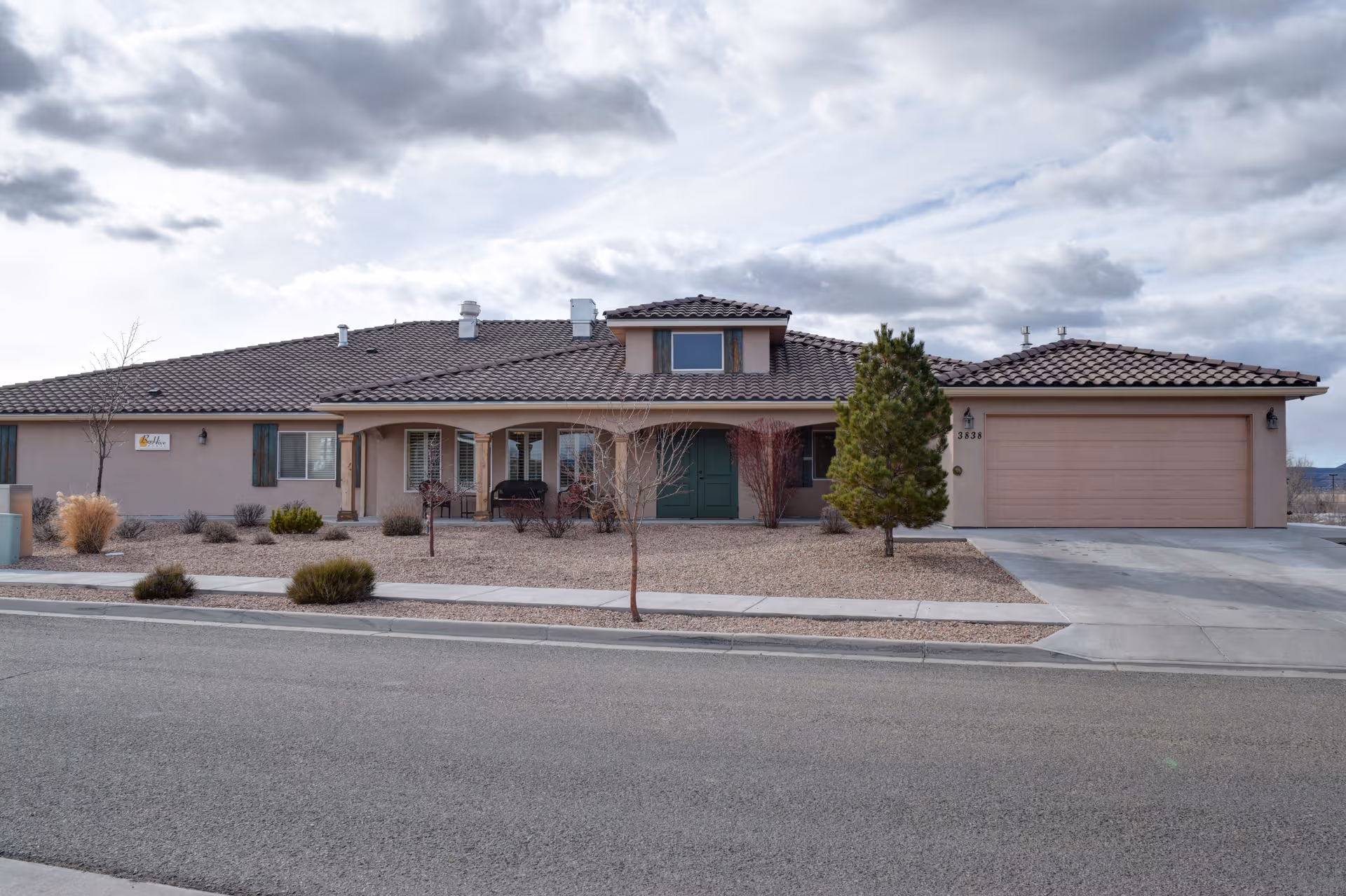 Single-story beige facility building with a green entrance, desert landscape, and attached garage.