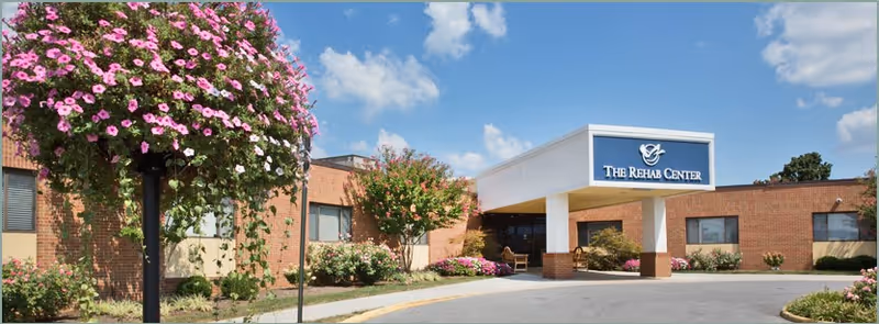 Front entrance of a brick rehab center with a covered drive-up canopy and landscaped flowers.