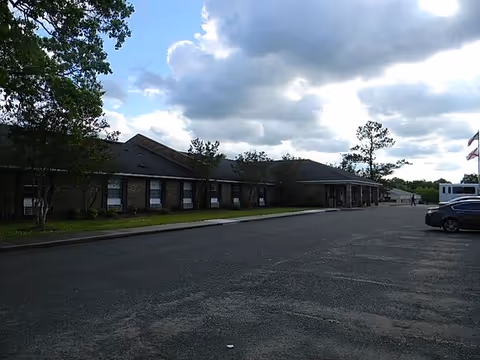 Single-story brick building exterior with windows and a parking lot under cloudy sky.