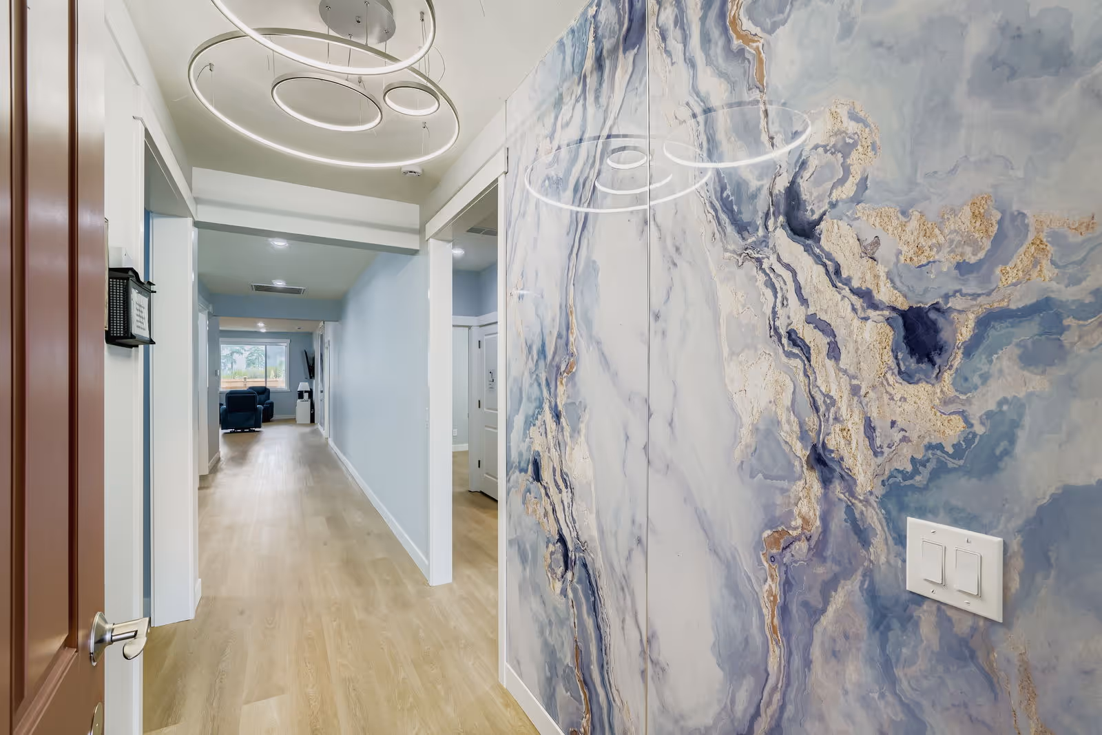Wide hallway in a modern senior living facility with blue marble wall mural and circular lights.