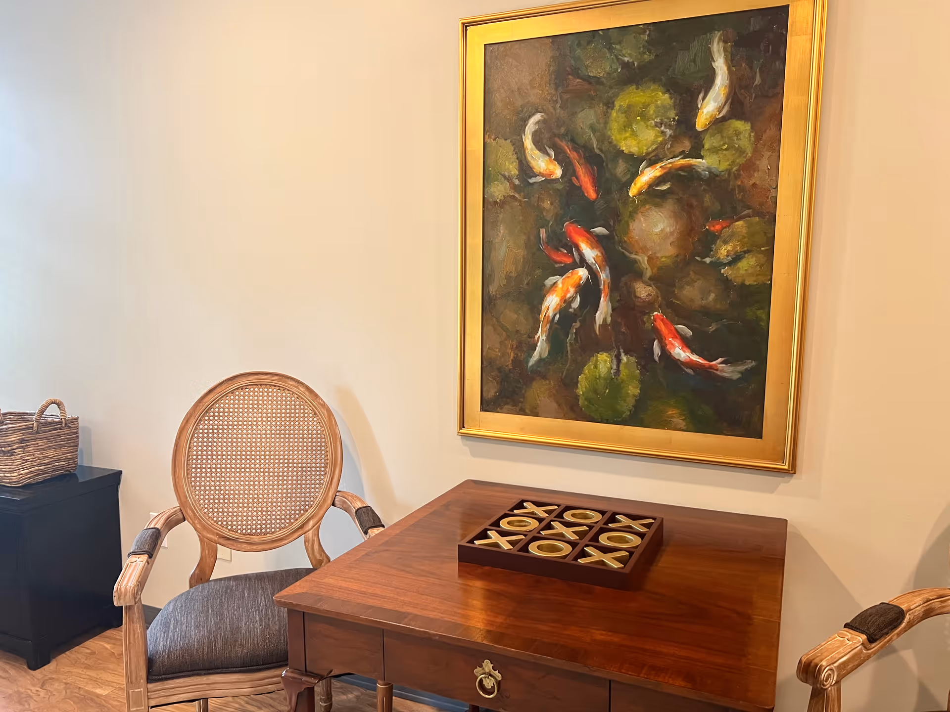 A wooden desk with two carved chairs in a cozy lounge beside a large koi painting.