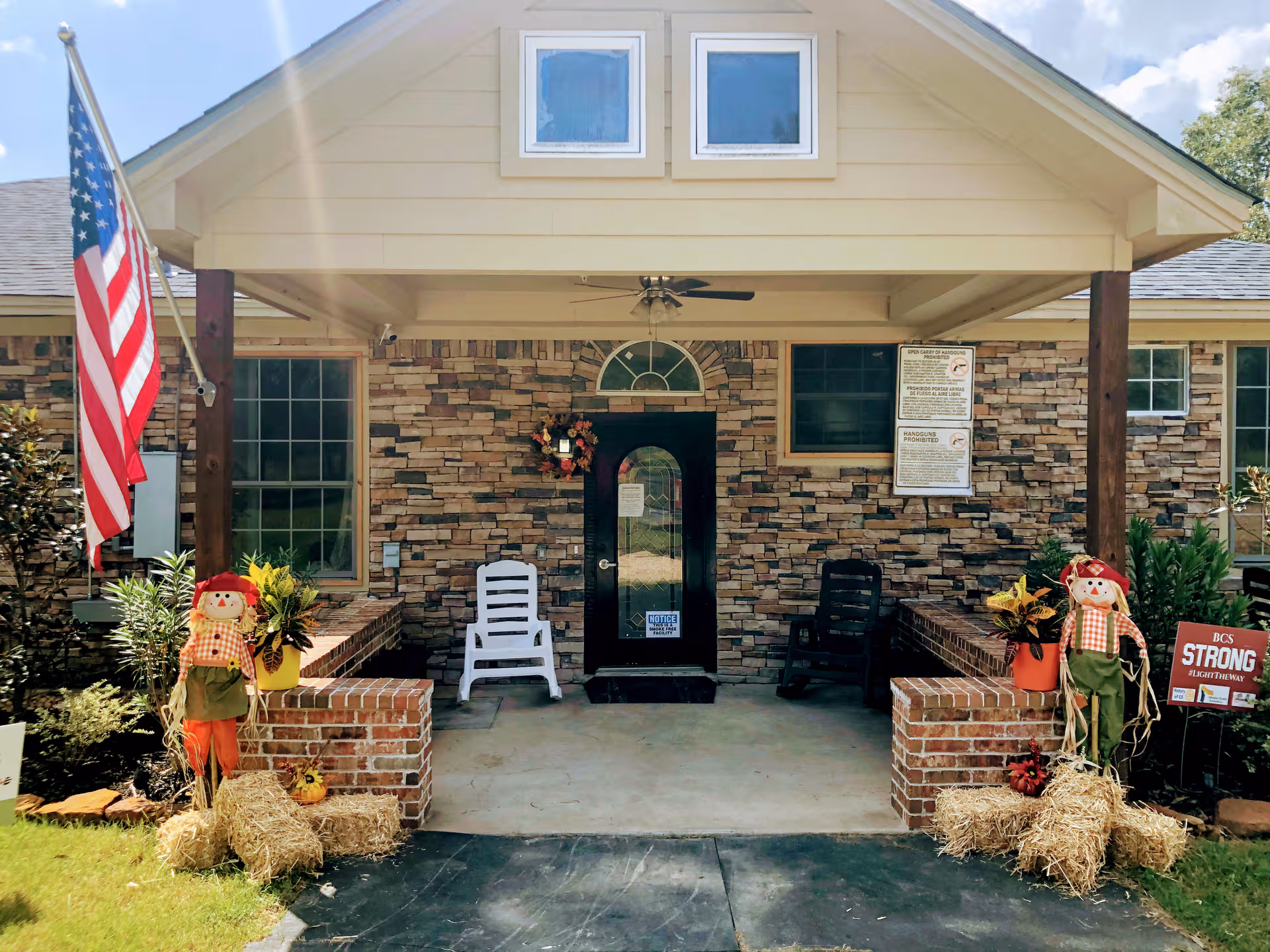 Front entrance of Peach Creek Assisted Living with brick facade, porch, flag, and autumn decorations.