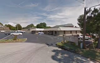 A single-story senior living facility exterior with a parking lot and several parked cars.