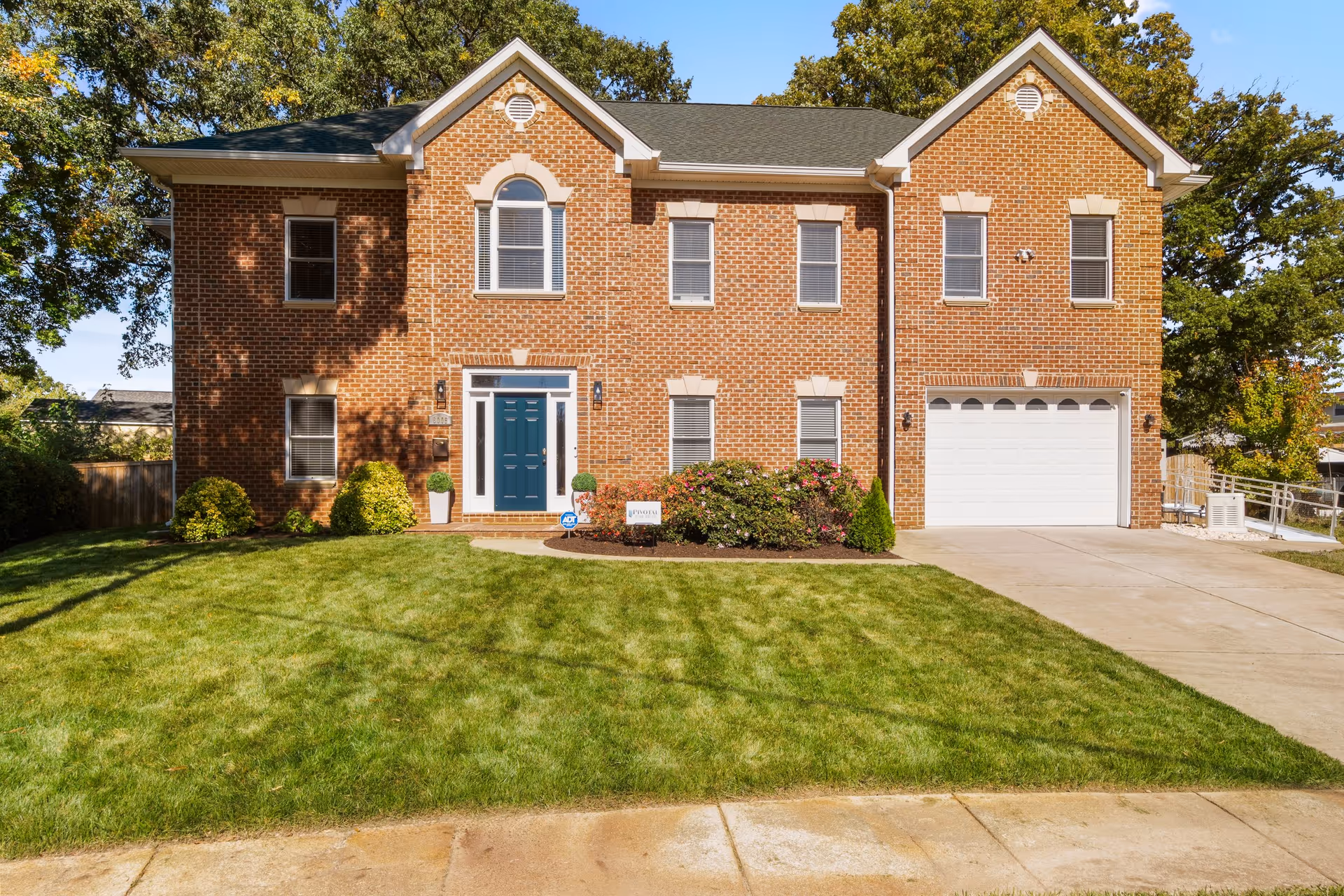 Brick two-story senior living facility front with manicured lawn, driveway, and attached garage.