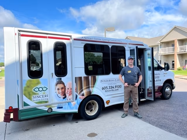 Ponderosa Lodge Senior Living bus parked outside with a staff member nearby.