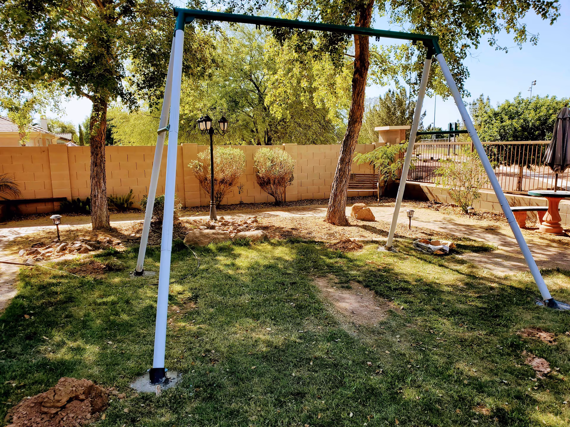 Outdoor backyard with a swing set, trees, rocks, and a beige privacy wall.