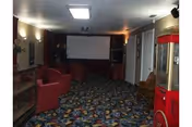 Indoor lounge area with red chairs, patterned carpet, and a projector screen at the far end.