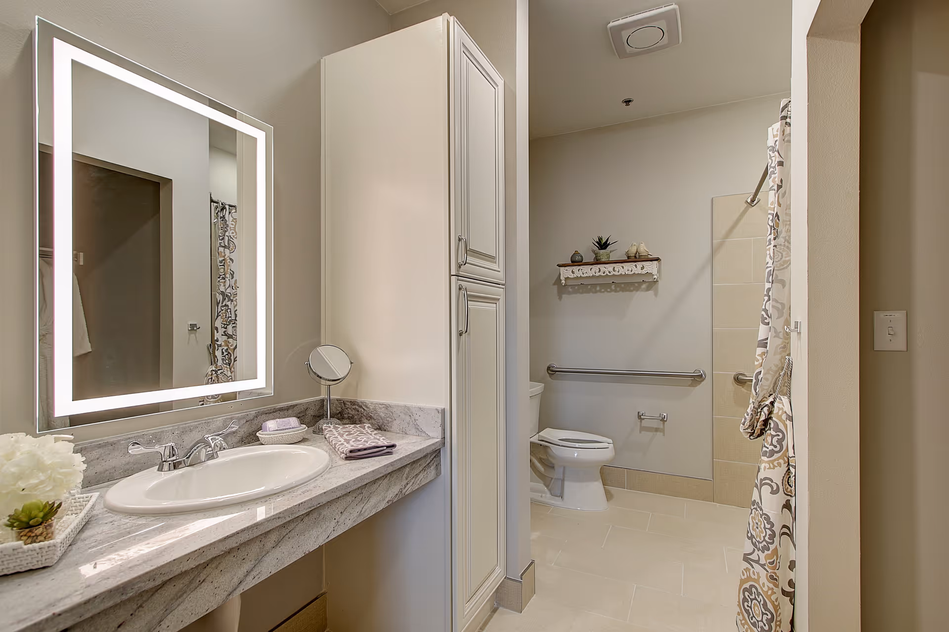 Bright bathroom featuring a marble countertop sink, illuminated mirror, and accessible shower.