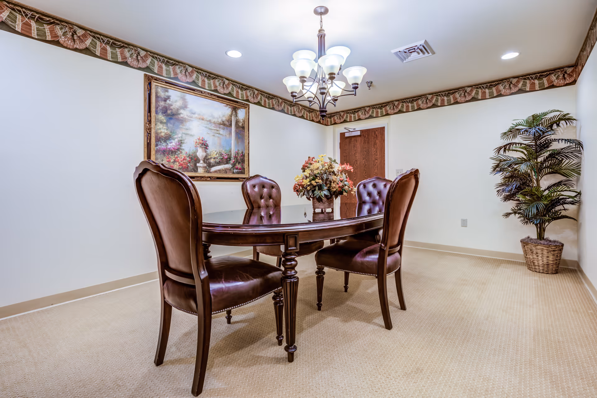 Formal dining room with dark wood table, leather chairs, chandelier, painting, and potted plant.