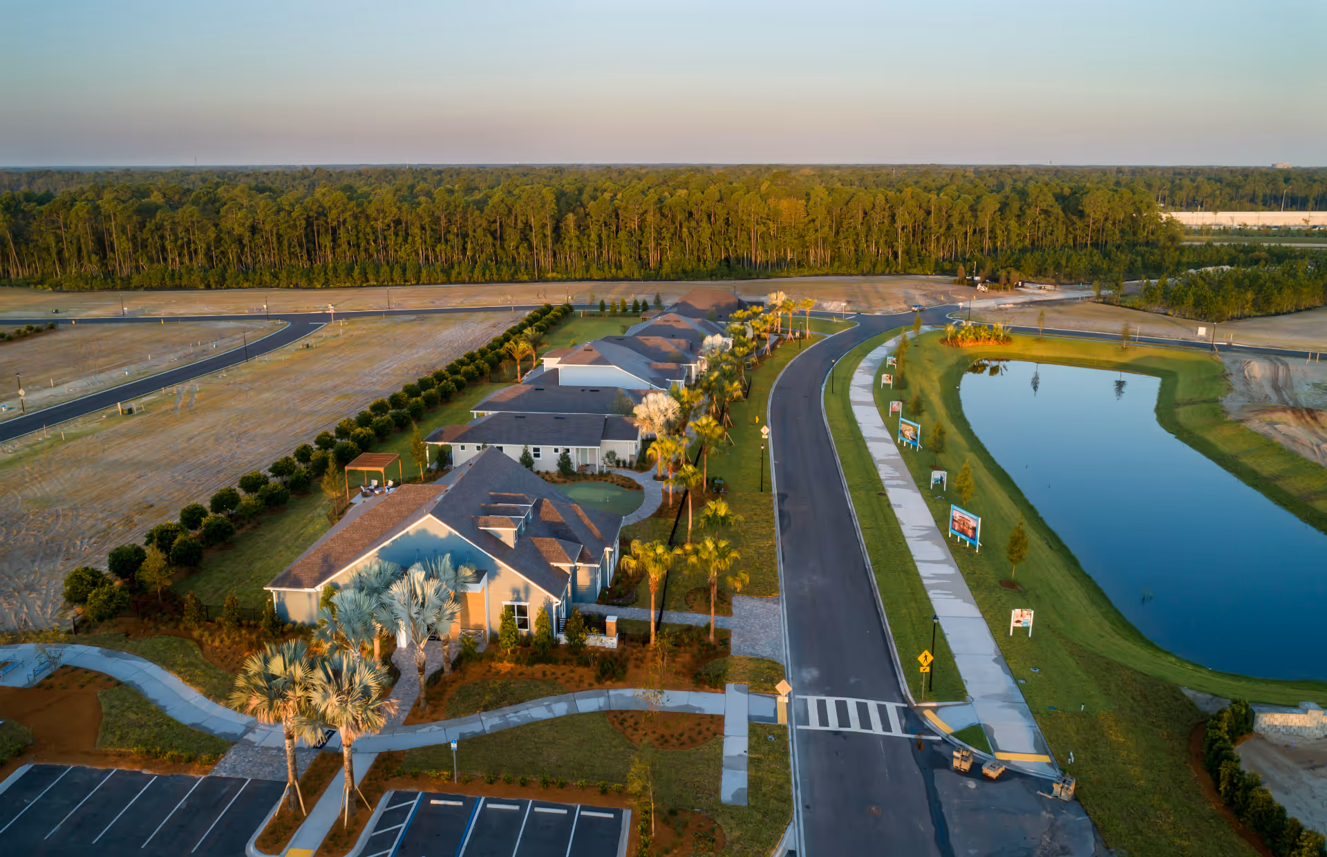 Aerial view of a senior living community with buildings, roads, palm trees, and a pond