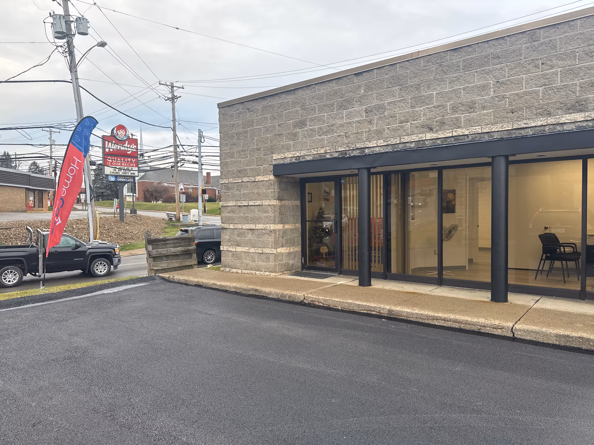 Exterior view of a brick building with glass doors and parking area.