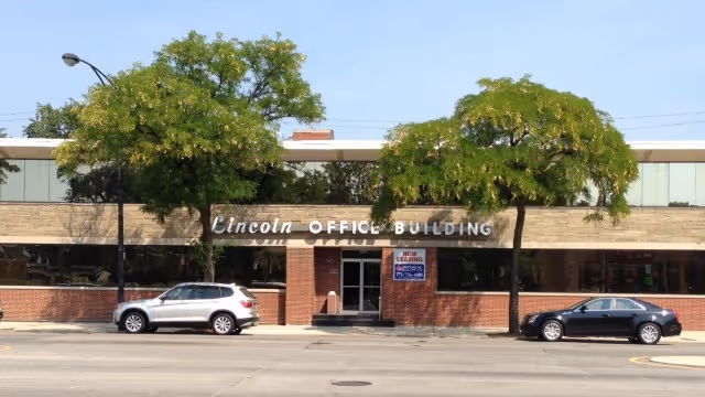 Exterior view of Lincoln Office Building storefront with two parked cars and trees