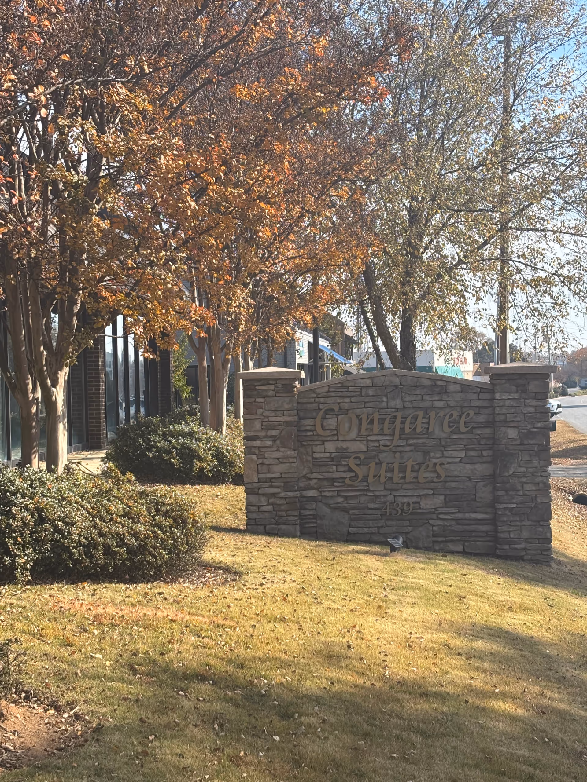 Stone entrance sign with autumn trees and manicured landscaping near a senior living campus.