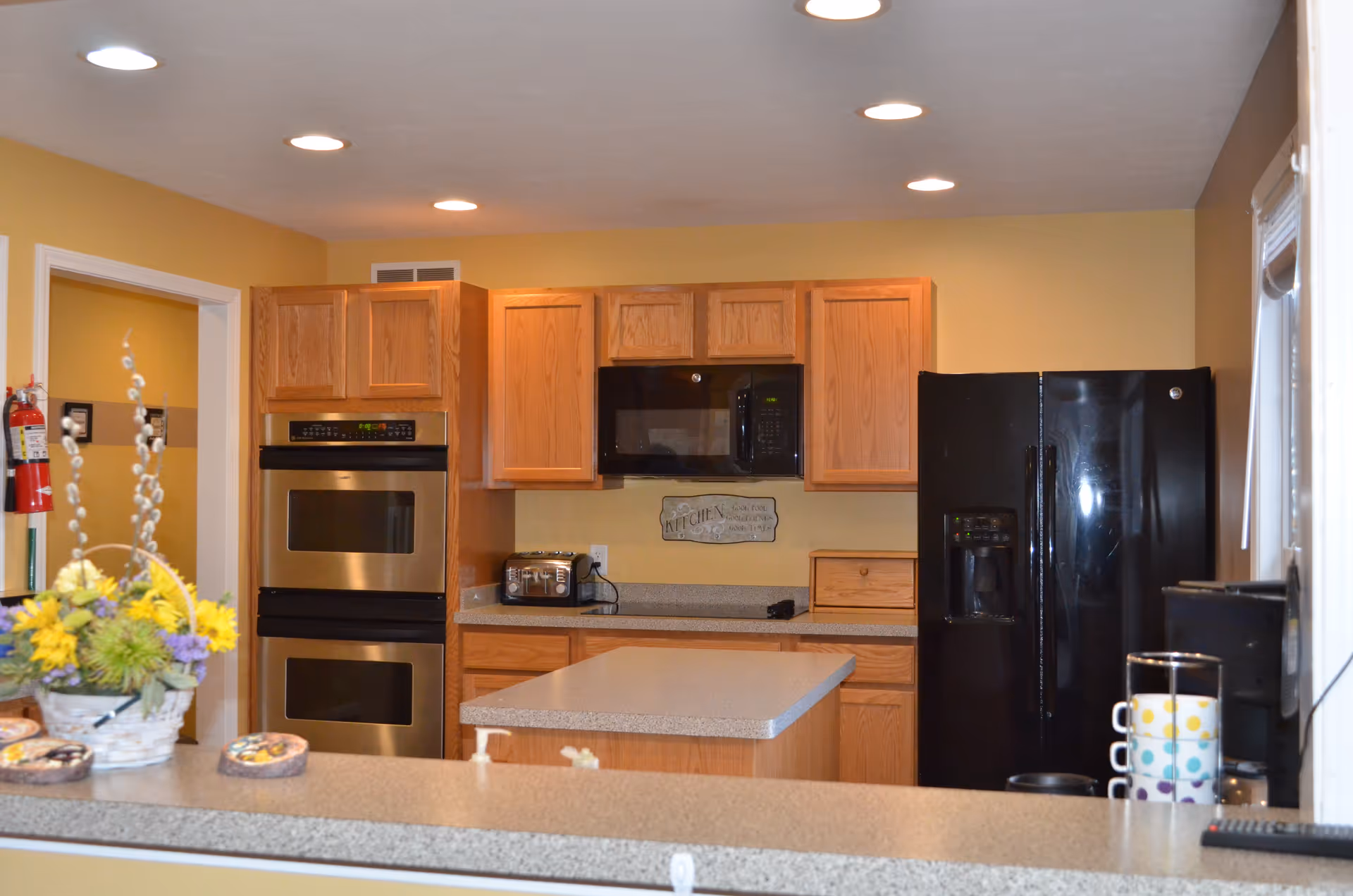 Bright yellow kitchen with wooden cabinets, a central island, and black appliances.