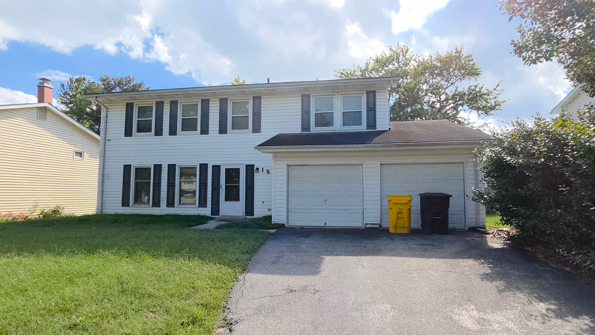 Two-story white house with a two-car garage, black shutters, and a paved driveway.