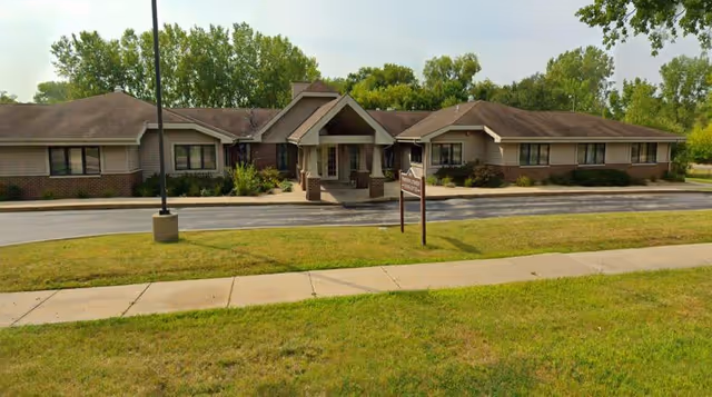 Single-story senior living building with a covered entrance, front driveway, and a grassy lawn.