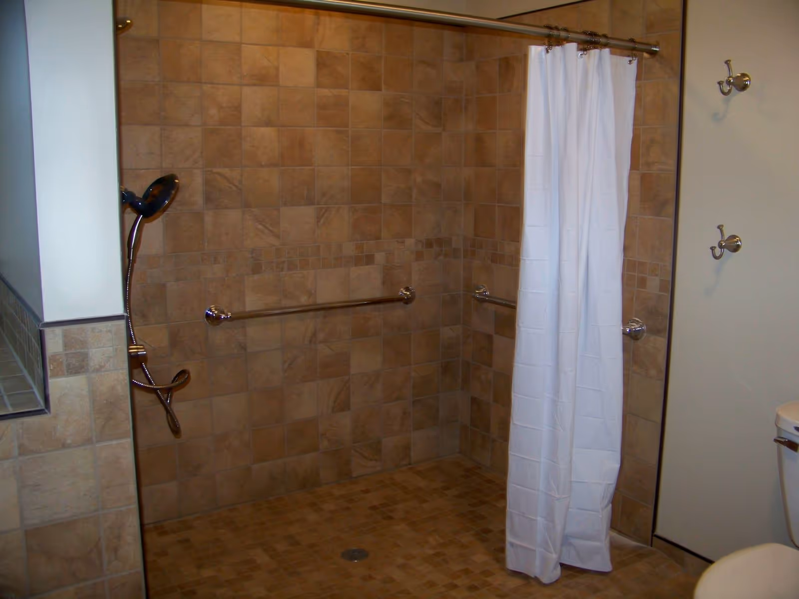 Tiled walk-in shower with grab bars and a white shower curtain.